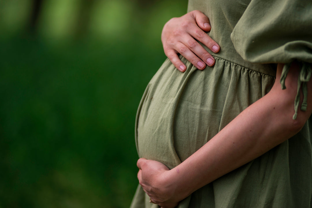 Schwangere Frau hält ihren Babybauch in einem grünen Kleid