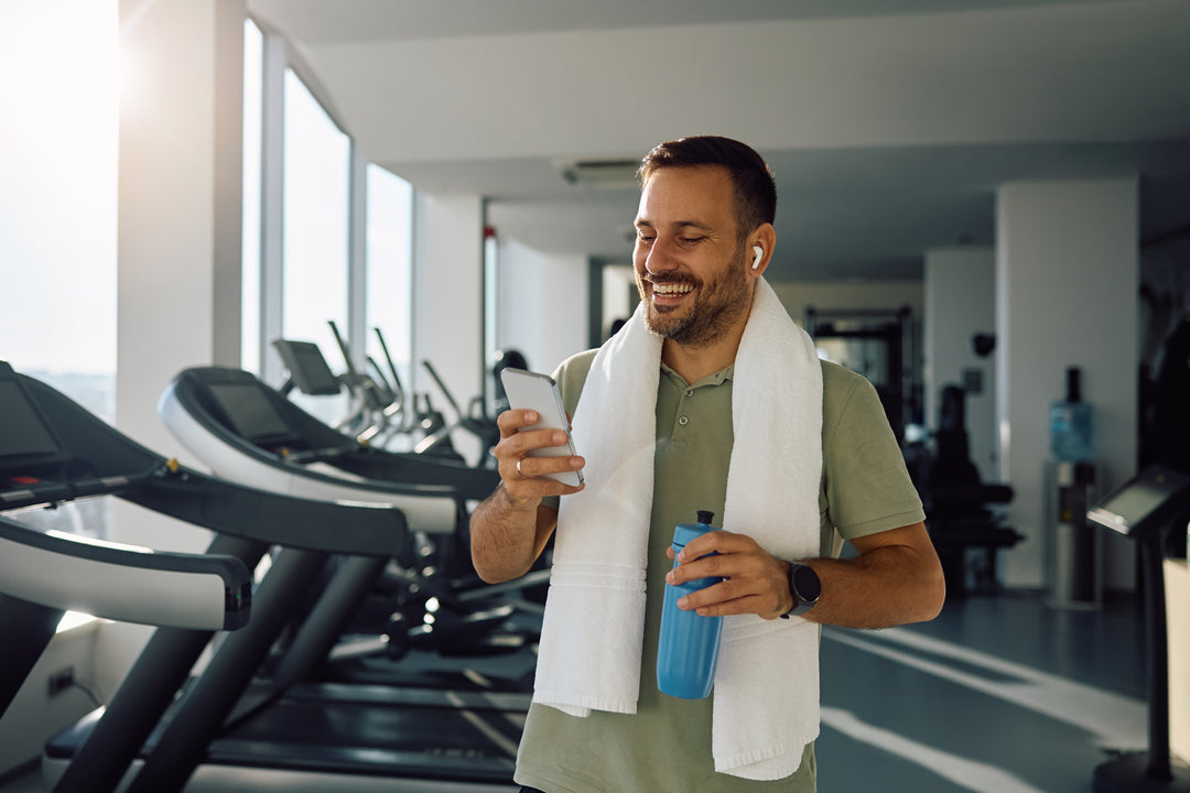 Mann im Fitnessstudio sieht glücklich aus nach dem Training und tippt am Handy